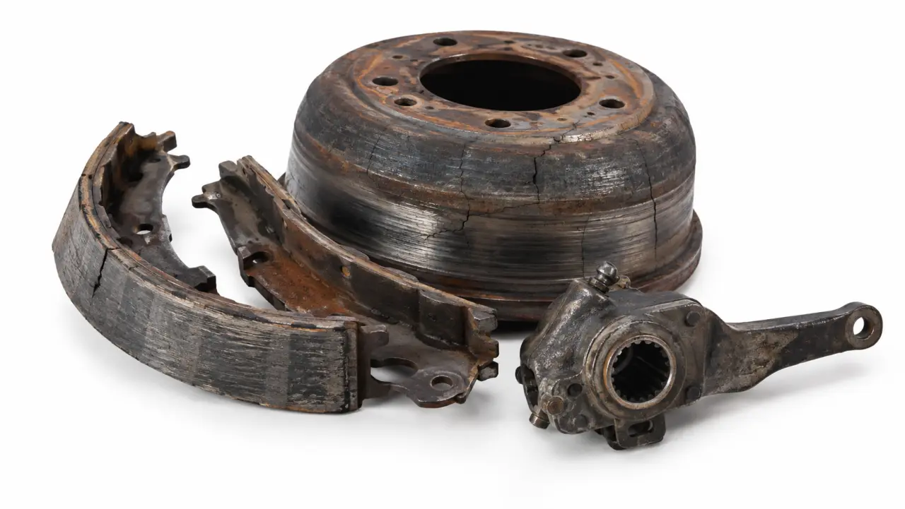 Close-up of worn truck brake shoes and a cracked drum on a workshop bench
